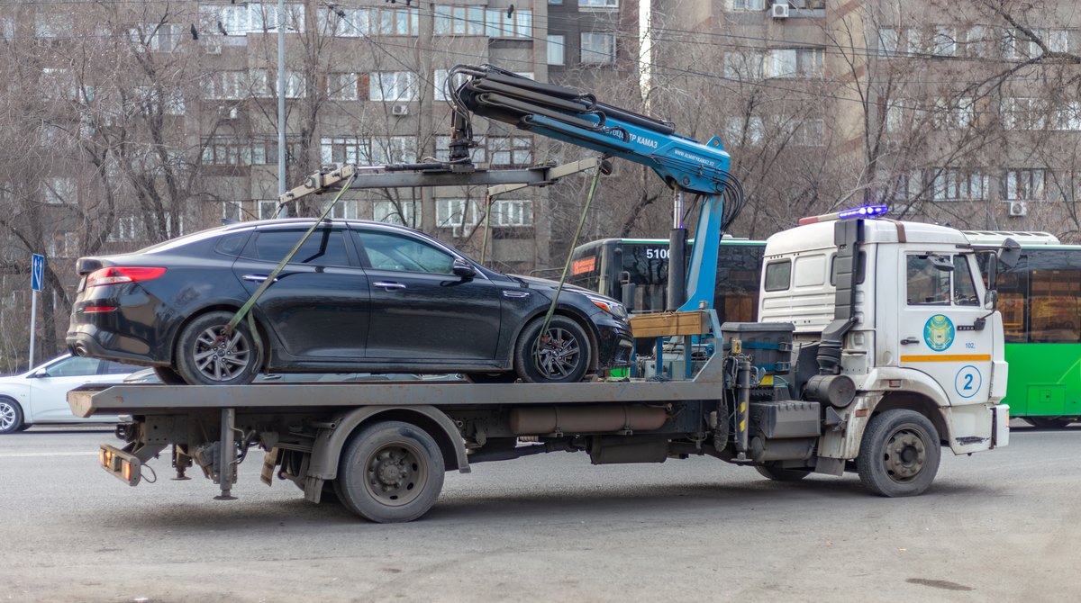Эвакуатор полиции увозит легковой автомобиль на улице Алматы