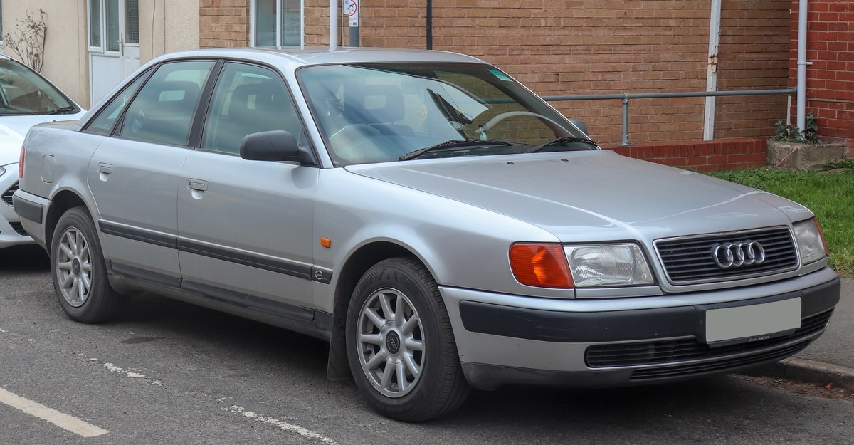 Серебристый Audi 100 C4, вид спереди справа в три четверти, у кирпичной стены