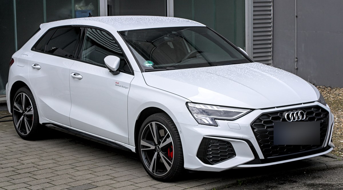 Белый Audi A3 Sportback, вид спереди справа, на мощёной площадке у здания