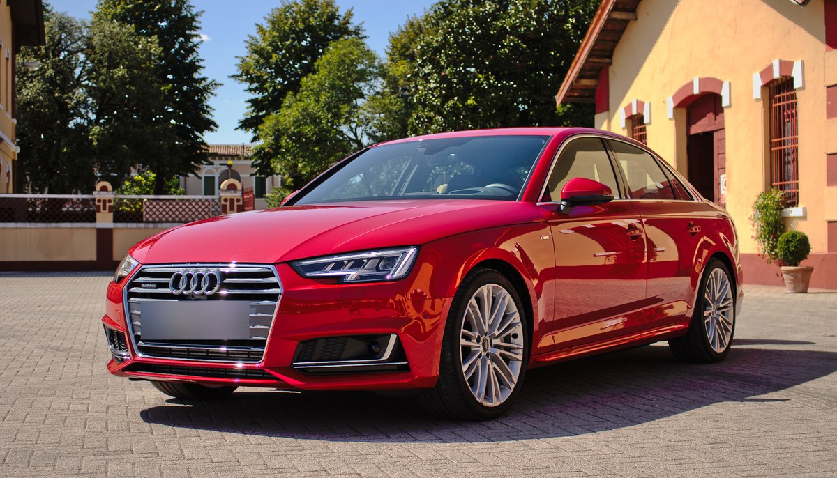 Красный седан Audi A4 B9 S line, вид спереди слева, на брусчатке