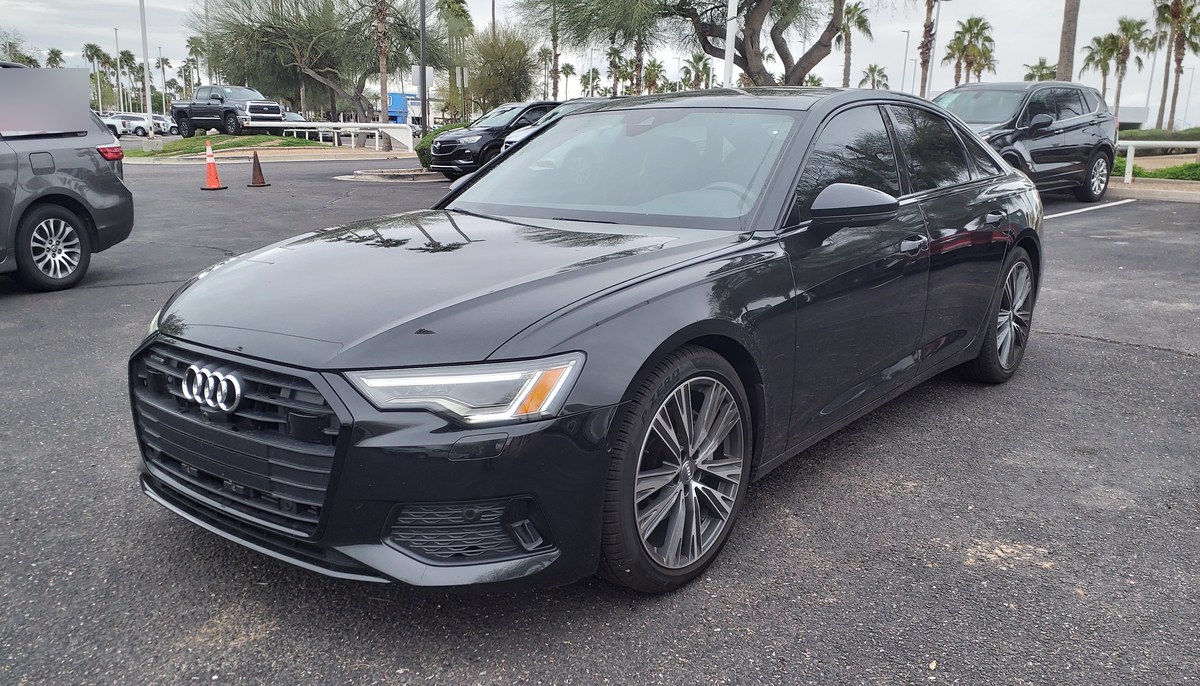 Чёрный седан Audi A6 C8, вид спереди слева, на стоянке дилера