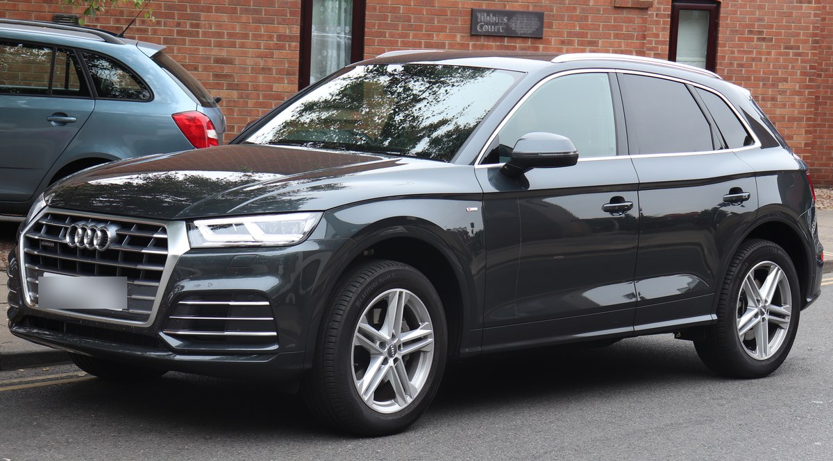 Тёмно-серый Audi Q5 второго поколения S line, вид спереди слева, у кирпичного здания