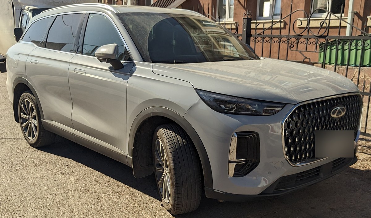 Серый Chery Tiggo 9, вид спереди справа, на улице у забора