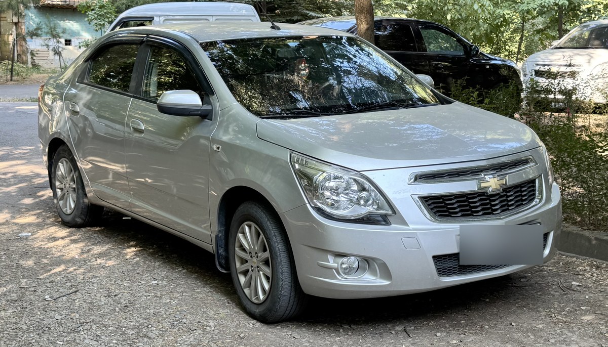 Серебристый седан Chevrolet Cobalt узбекской сборки, вид спереди сбоку, на городском проспекте
