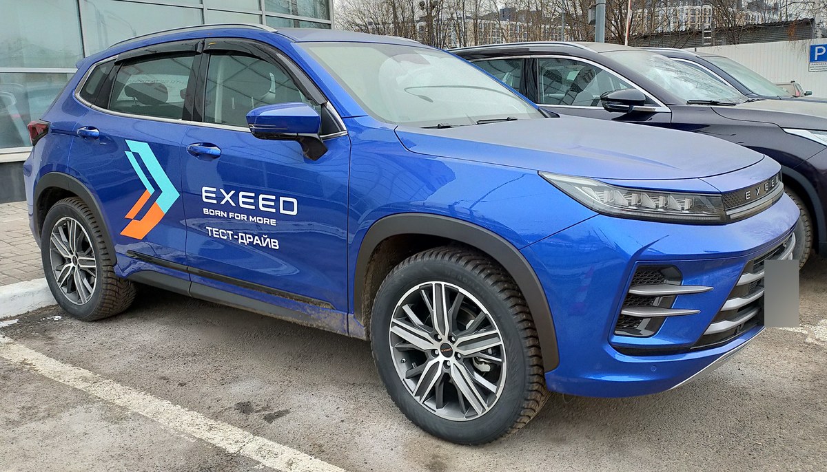 Синий Exeed LX в тест-драйвной ливрее дилера, вид спереди справа, на парковке