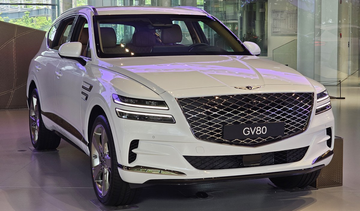 Белый Genesis GV80 первого поколения, вид спереди в три четверти, в автосалоне