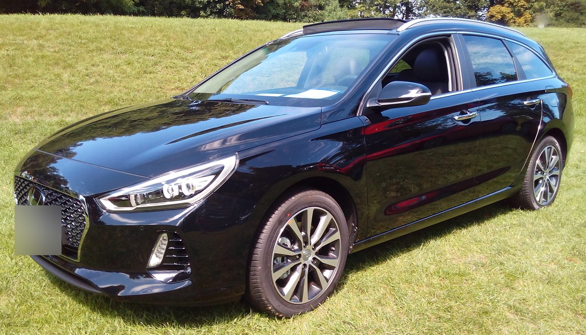 Чёрный Hyundai i30 универсал на выставке, вид спереди слева, на траве