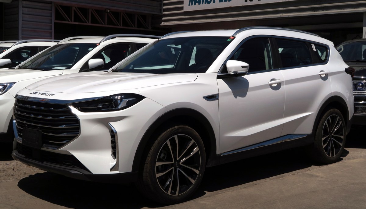 Белый кроссовер Jetour X70 Plus, вид спереди слева, на площадке автосалона