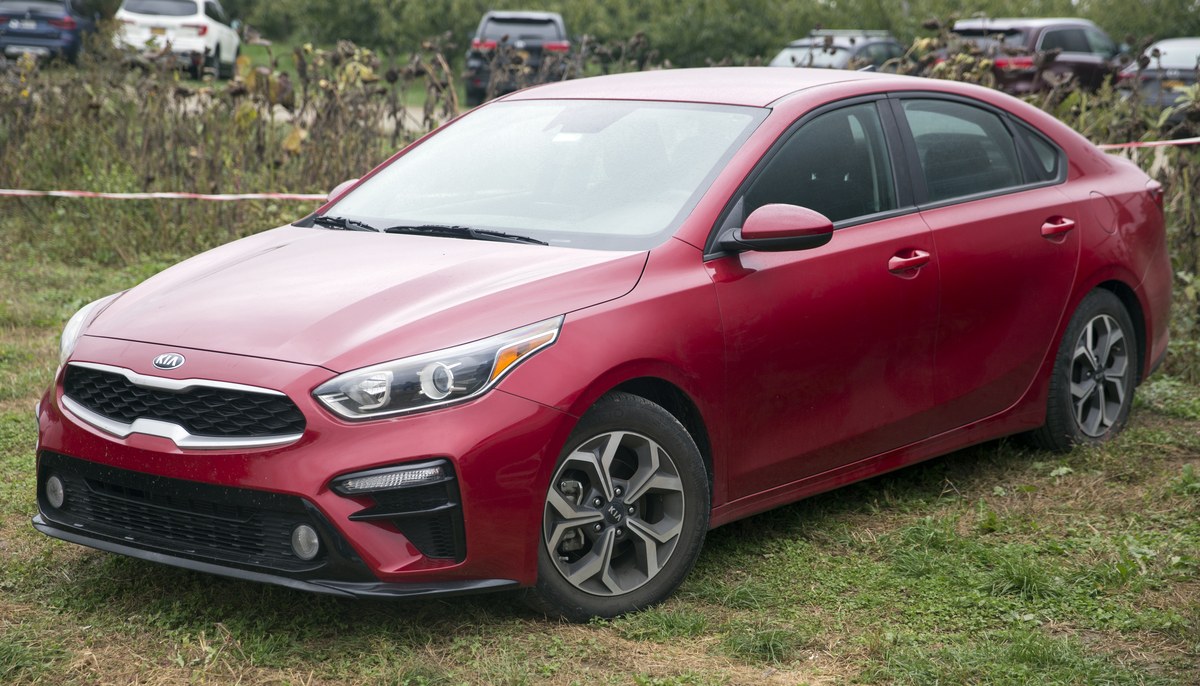 Красный седан Kia Forte (Cerato) третьего поколения BD на траве, вид спереди слева