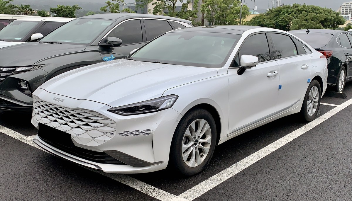 Белый седан Kia K8 (GL3) 2021 года выпуска, вид спереди в три четверти на парковке