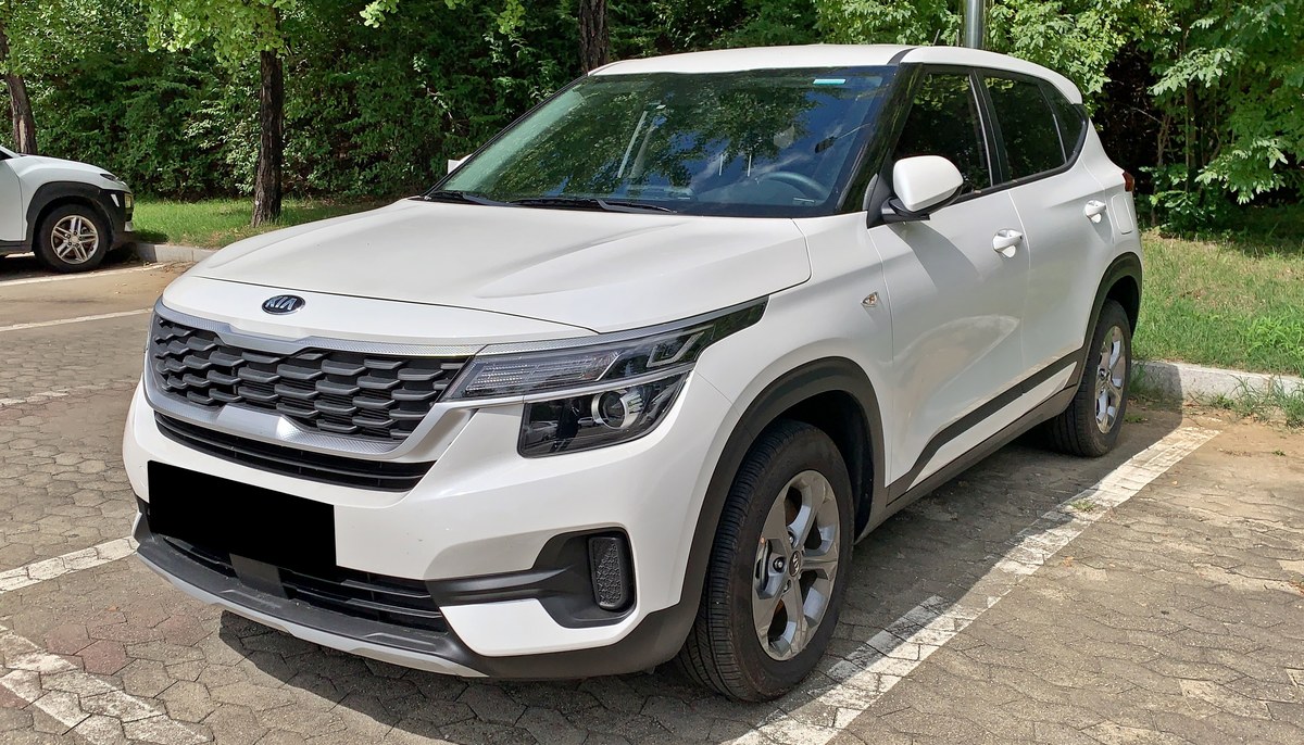 Белый компактный кроссовер Kia Seltos первого поколения SP2 на парковке, вид спереди слева