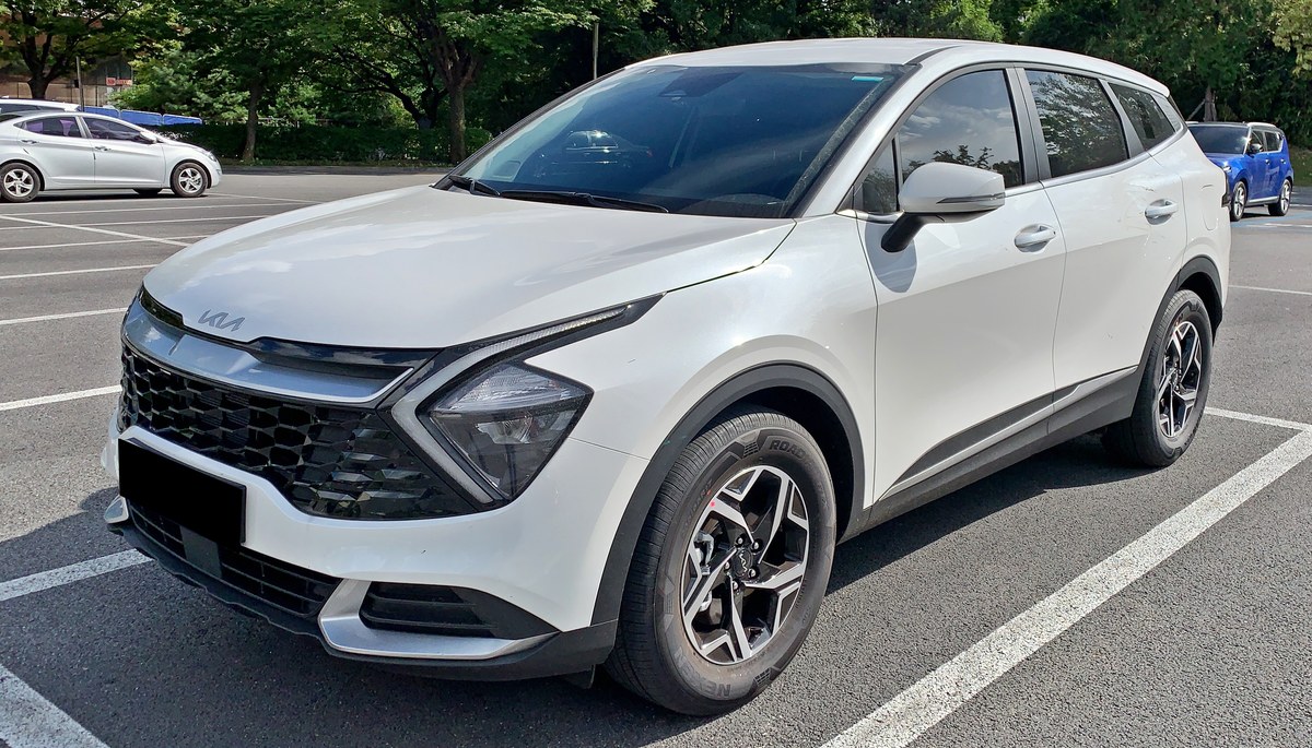 Белый кроссовер Kia Sportage пятого поколения NQ5 на парковке, вид спереди слева