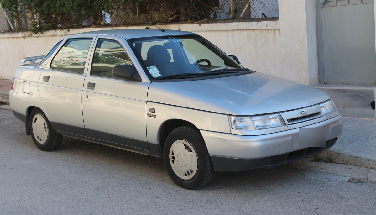 Серебристый седан ВАЗ-2110 (Lada 110) первых лет выпуска, вид спереди сбоку, экспортная версия на улице в Греции
