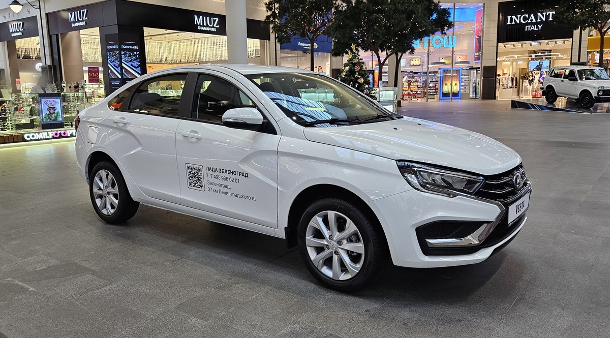 Белый седан Lada Vesta NG со светодиодной оптикой, вид спереди сбоку, на выставочной площадке торгового центра