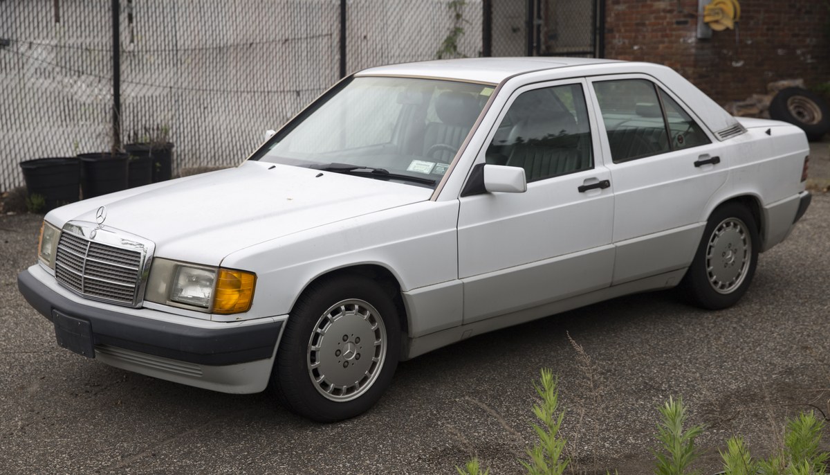 Белый Mercedes-Benz 190 E (W201) седан, вид спереди слева в три четверти, на асфальтовой площадке