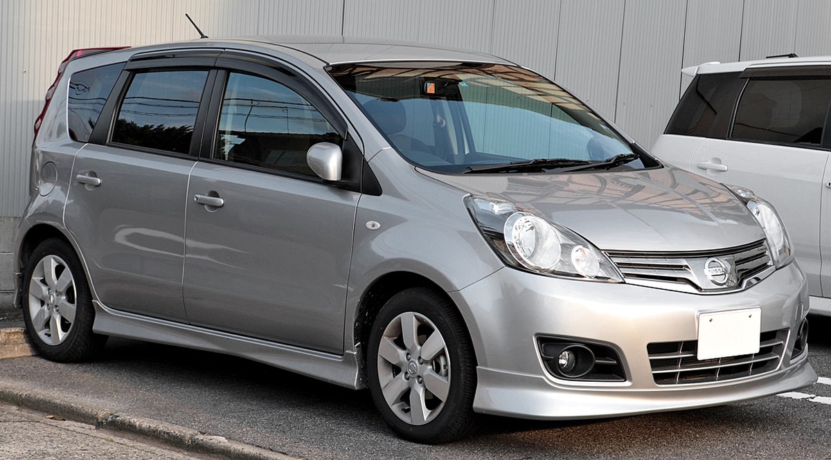Серебристый Nissan Note E11 после рестайлинга с обвесом, вид спереди слева в три четверти, на парковке