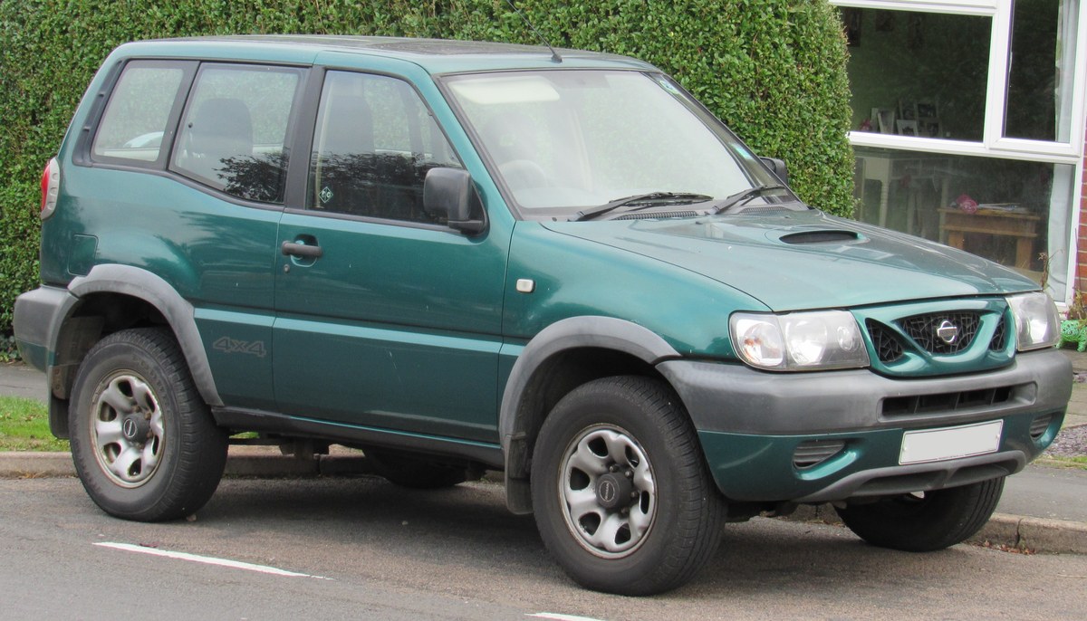 Зелёный Nissan Terrano II после рестайлинга, 3-дверный внедорожник, вид спереди справа в три четверти, у живой изгороди на улице