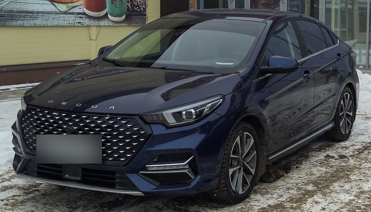 Тёмно-синий седан Omoda S5, вид спереди сбоку, на заснеженной парковке у магазина