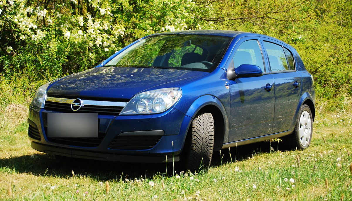 Синий Opel Astra H, пятидверный хэтчбек до рестайлинга, вид спереди сбоку, на траве