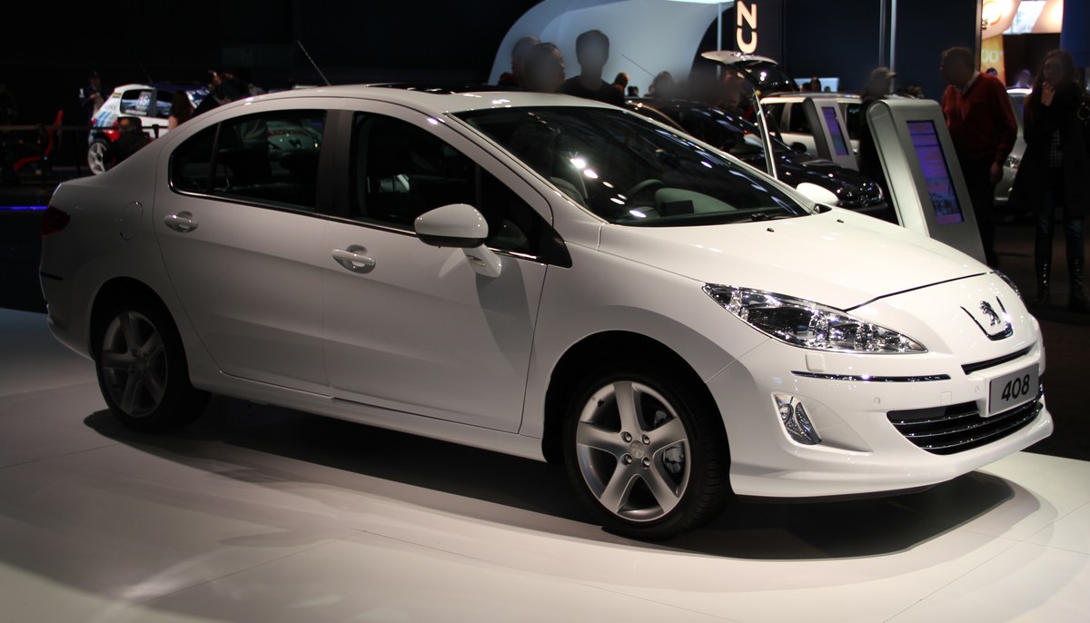 Белый седан Peugeot 408 Feline на стенде автосалона, вид спереди справа