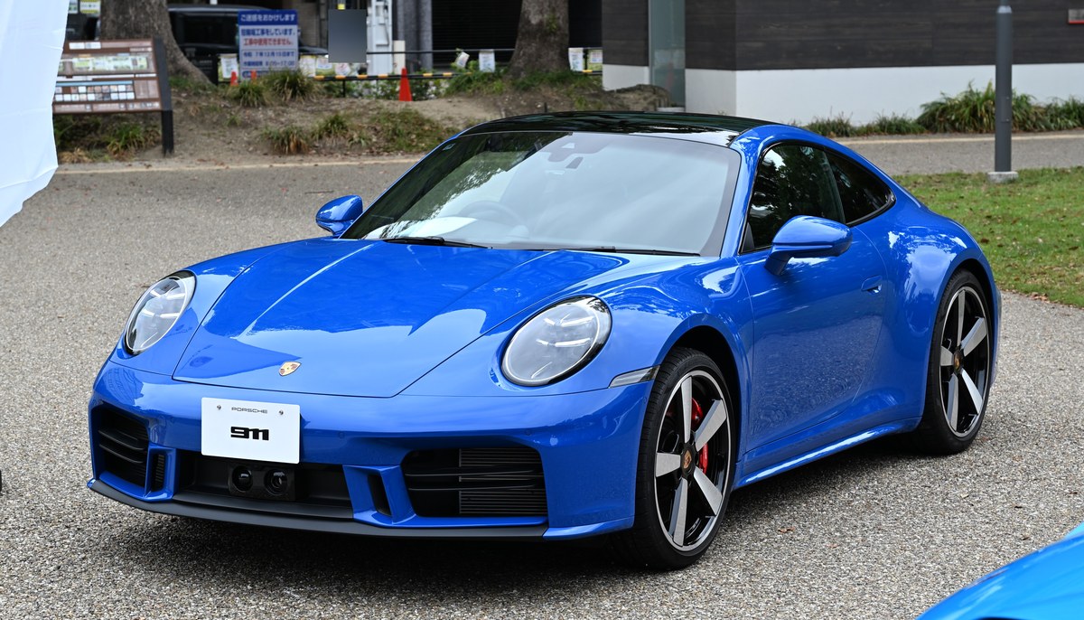 Синий Porsche 911 Carrera S поколения 992 в рестайлинговой версии, вид спереди слева, на площадке в Японии
