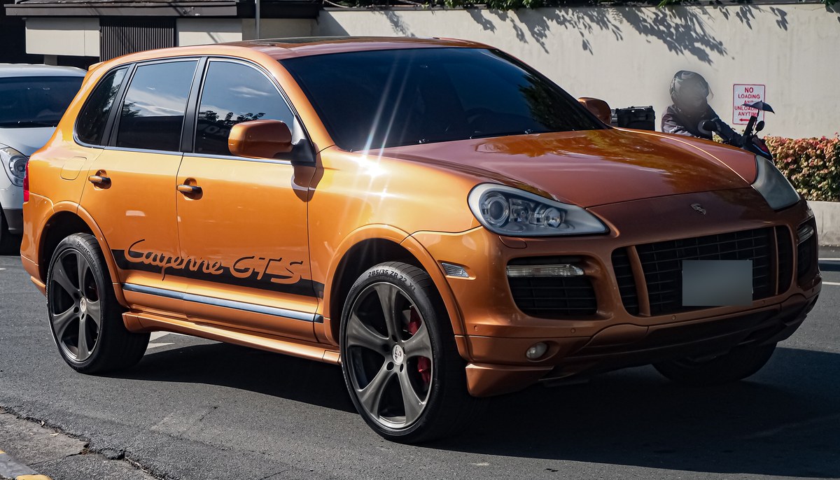 Оранжевый Porsche Cayenne GTS первого поколения, вид спереди в три четверти, на городской улице