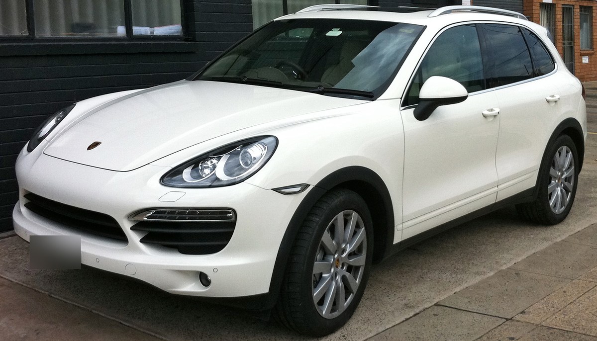 Белый Porsche Cayenne S второго поколения, вид спереди в три четверти, у кирпичной стены