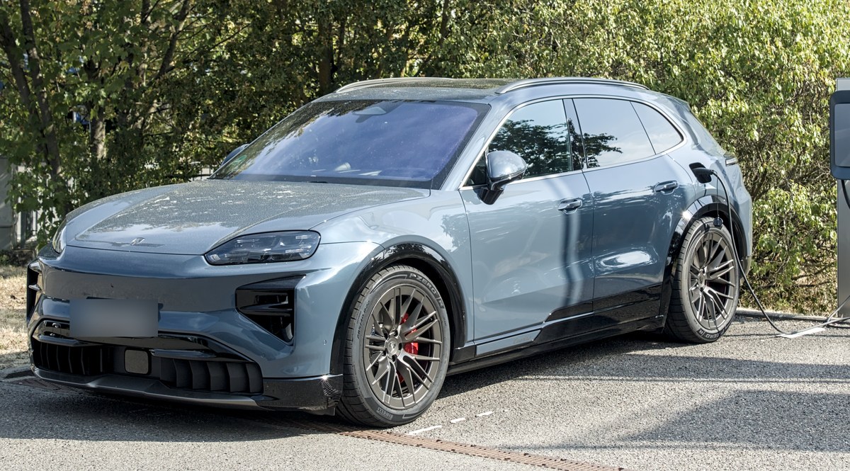 Porsche Cayenne Electric Turbo в серо-голубом цвете на зарядной станции, вид спереди в три четверти
