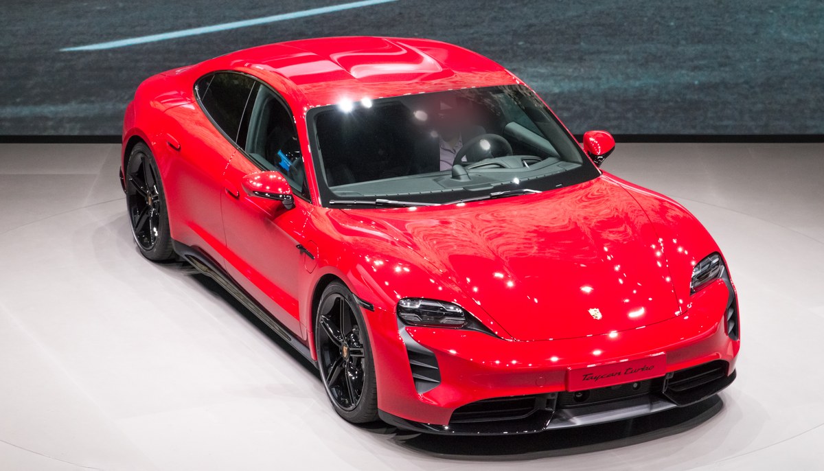 Красный Porsche Taycan Turbo первого поколения на сцене автосалона, вид спереди сверху слева