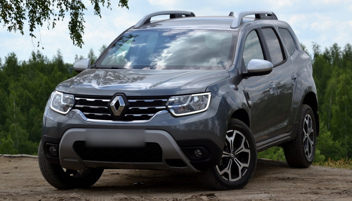 Серый Renault Duster второго поколения, вид спереди в три четверти, на фоне леса