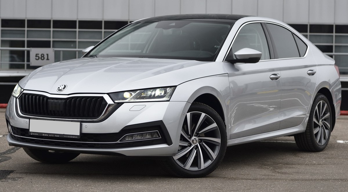 Серебристый лифтбек Skoda Octavia IV поколения, вид спереди в три четверти, на парковке у здания