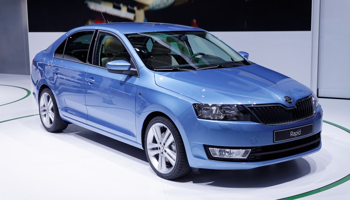 Голубой лифтбек Skoda Rapid первого поколения на стенде автосалона, вид спереди сбоку