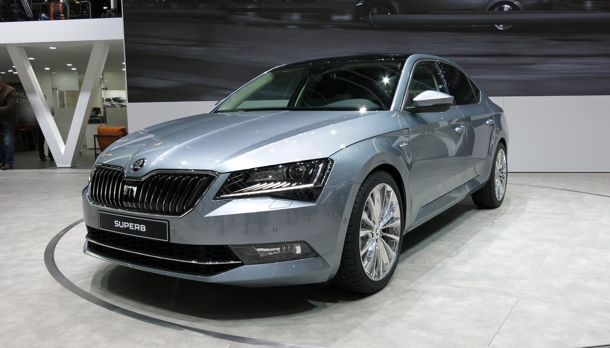 Серо-голубой лифтбек Skoda Superb третьего поколения на стенде автосалона, вид спереди сбоку