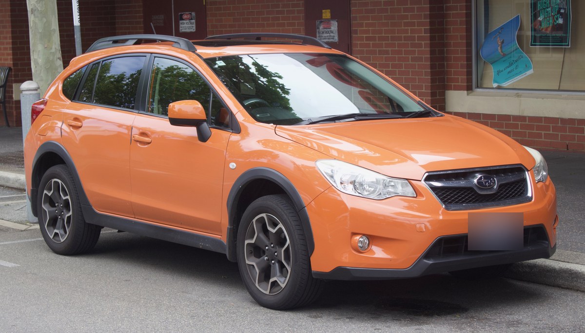 Оранжевый кроссовер Subaru XV первого поколения (GP), вид спереди-справа, у тротуара на городской улице