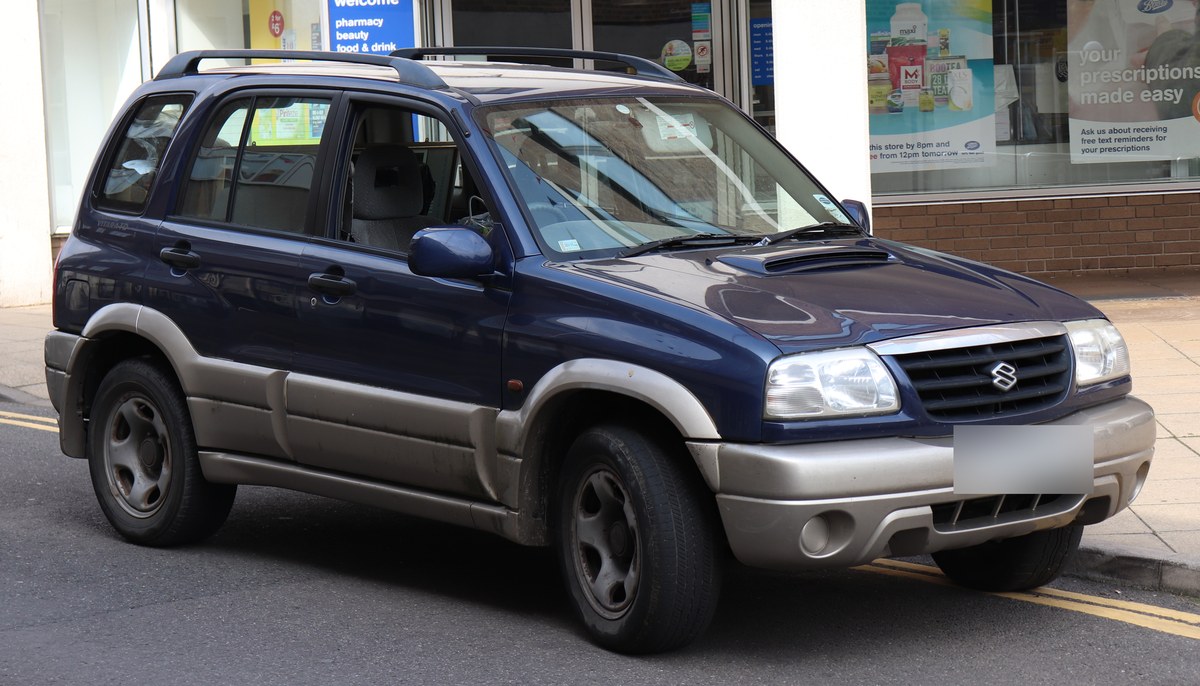 Синий Suzuki Grand Vitara первого поколения с серебристыми накладками, вид спереди справа, на городской улице