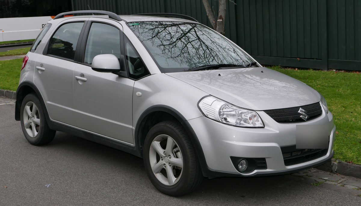 Серебристый Suzuki SX4 первого поколения, хэтчбек, вид спереди справа, у бордюра
