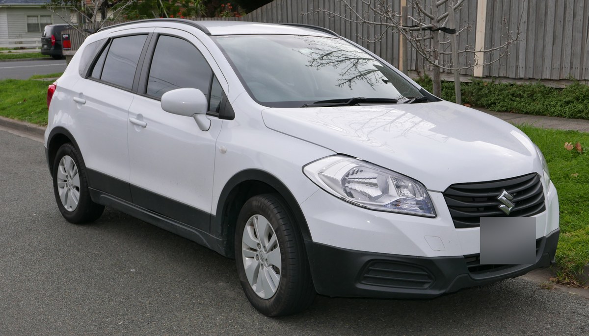 Белый Suzuki SX4 S-Cross первого поколения, вид спереди справа, припаркован у тротуара