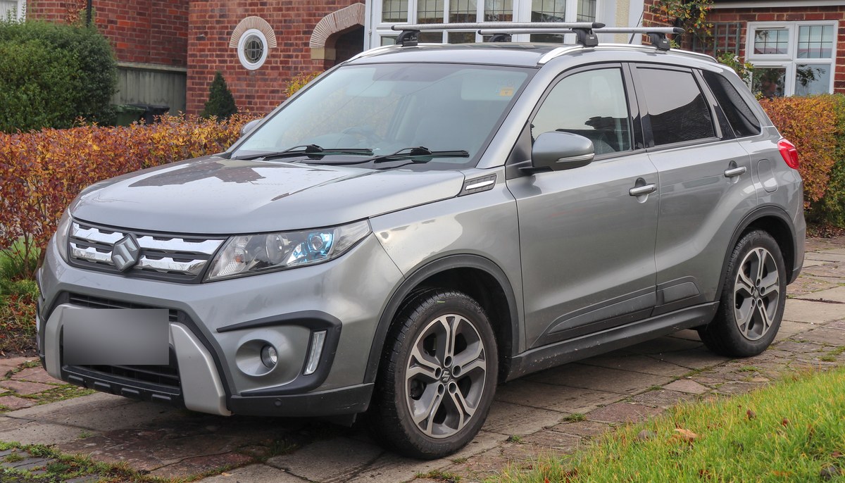 Серая Suzuki Vitara четвёртого поколения с багажными дугами на крыше, вид спереди сбоку
