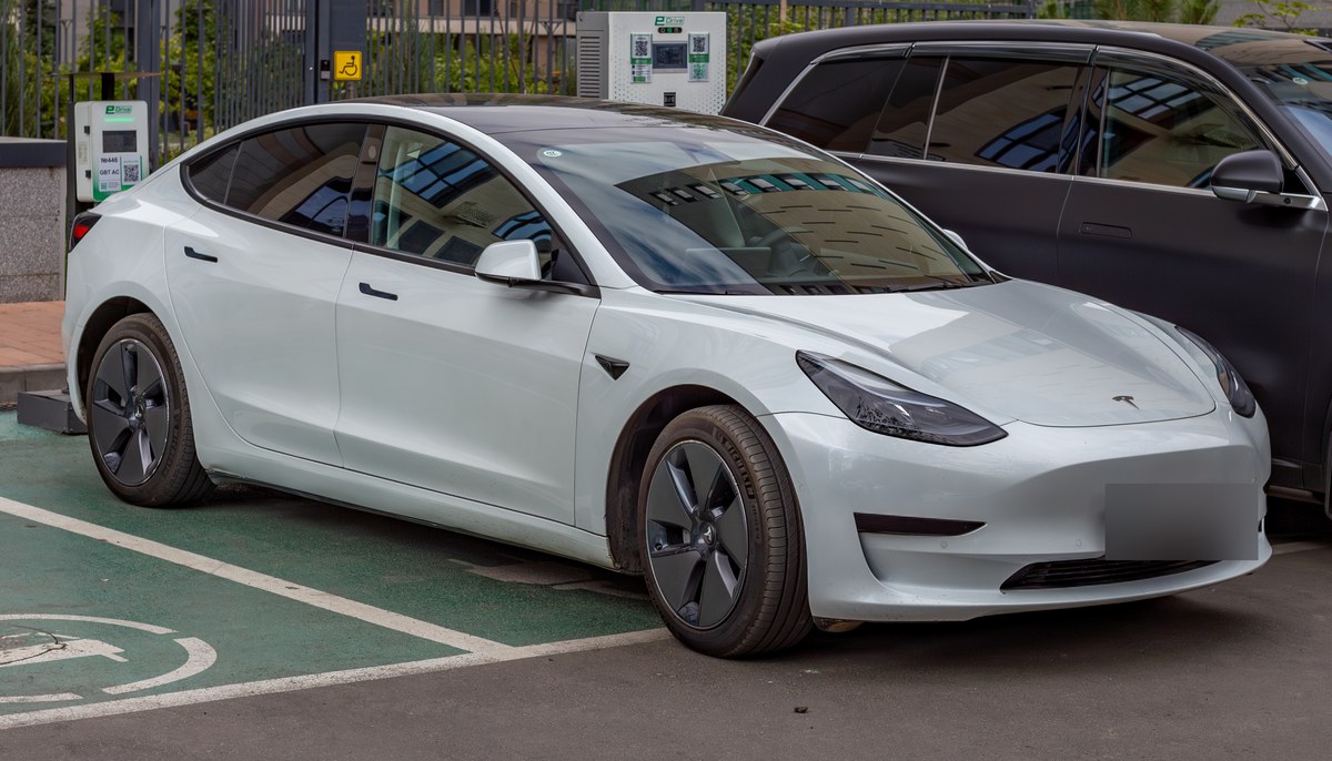 Белая Tesla Model 3 до обновления Highland на зарядной стоянке в Алматы, вид спереди сбоку