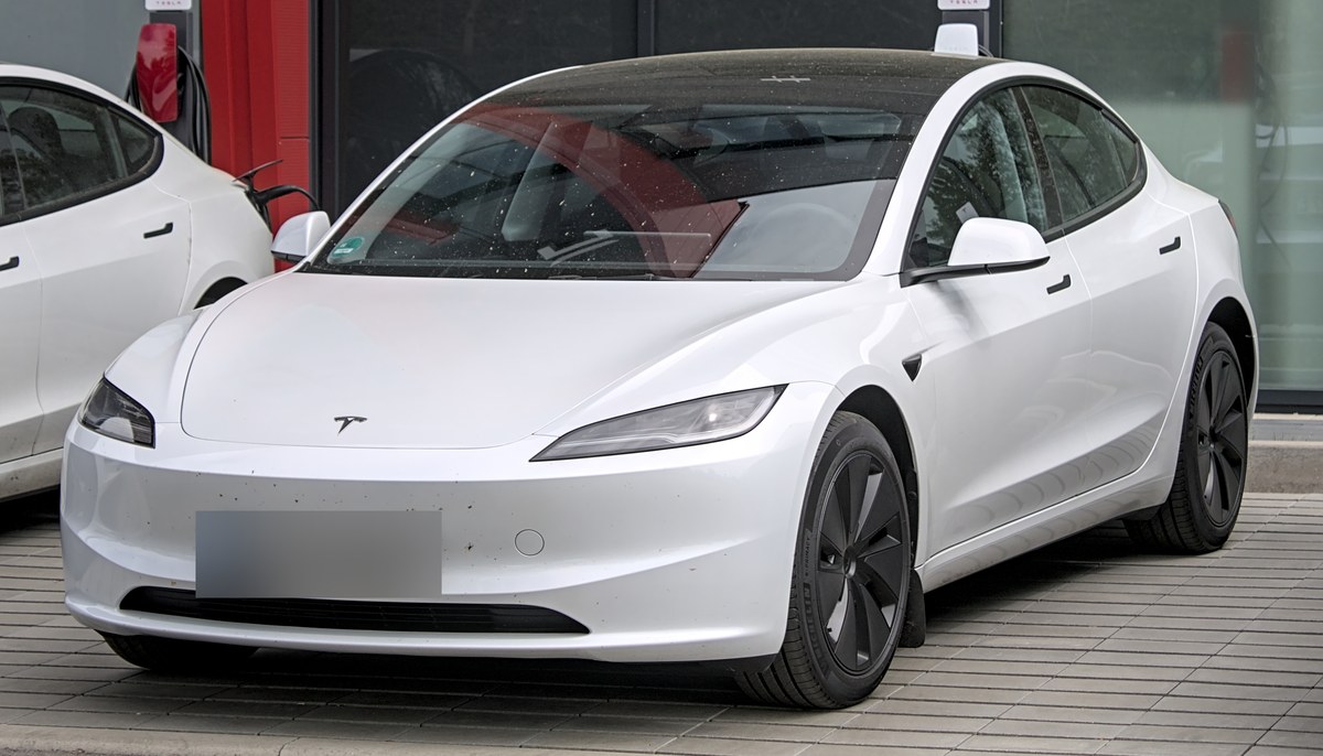Белая Tesla Model 3 Highland после обновления 2023 года, вид спереди сбоку, у зарядной станции в Германии