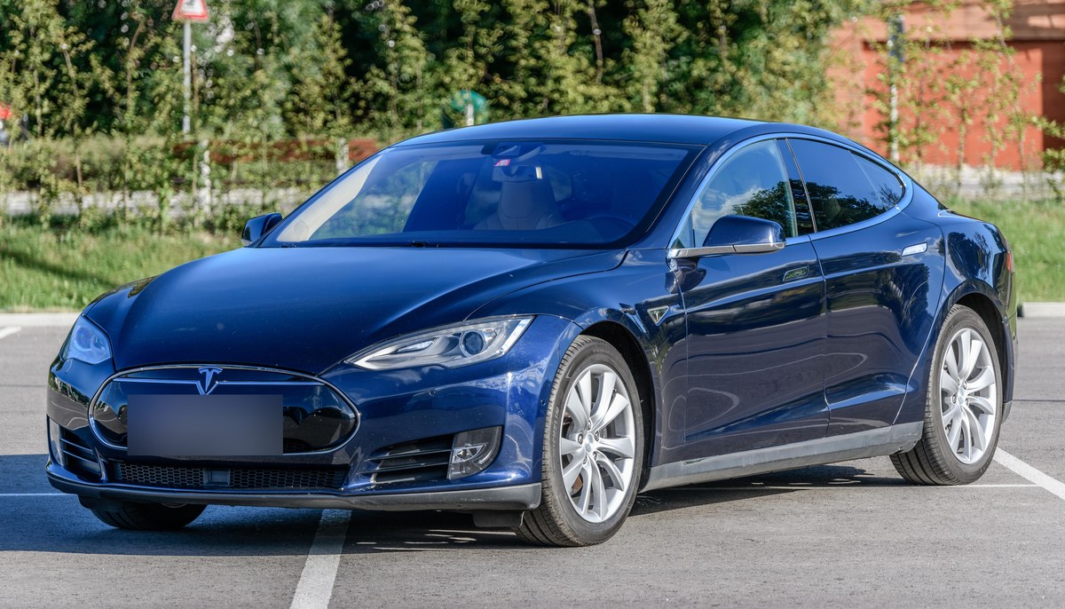 Синяя Tesla Model S первого поколения с решёткой-заглушкой на переднем бампере, вид спереди слева, на парковке