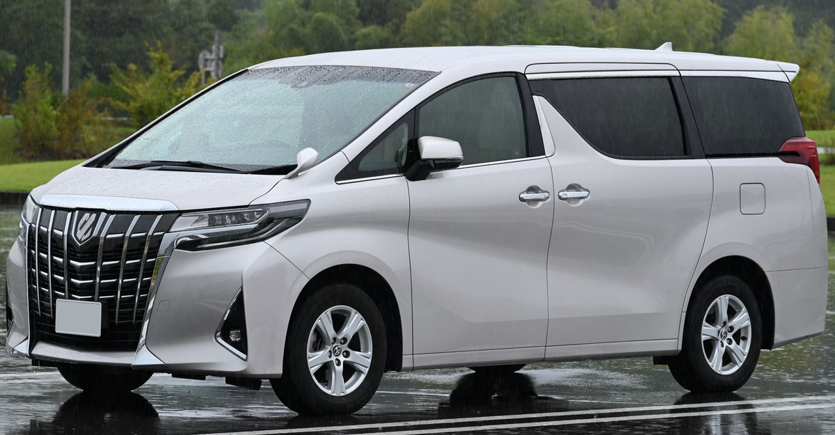 Белый Toyota Alphard AH30, вид спереди слева в три четверти, на мокрой парковке