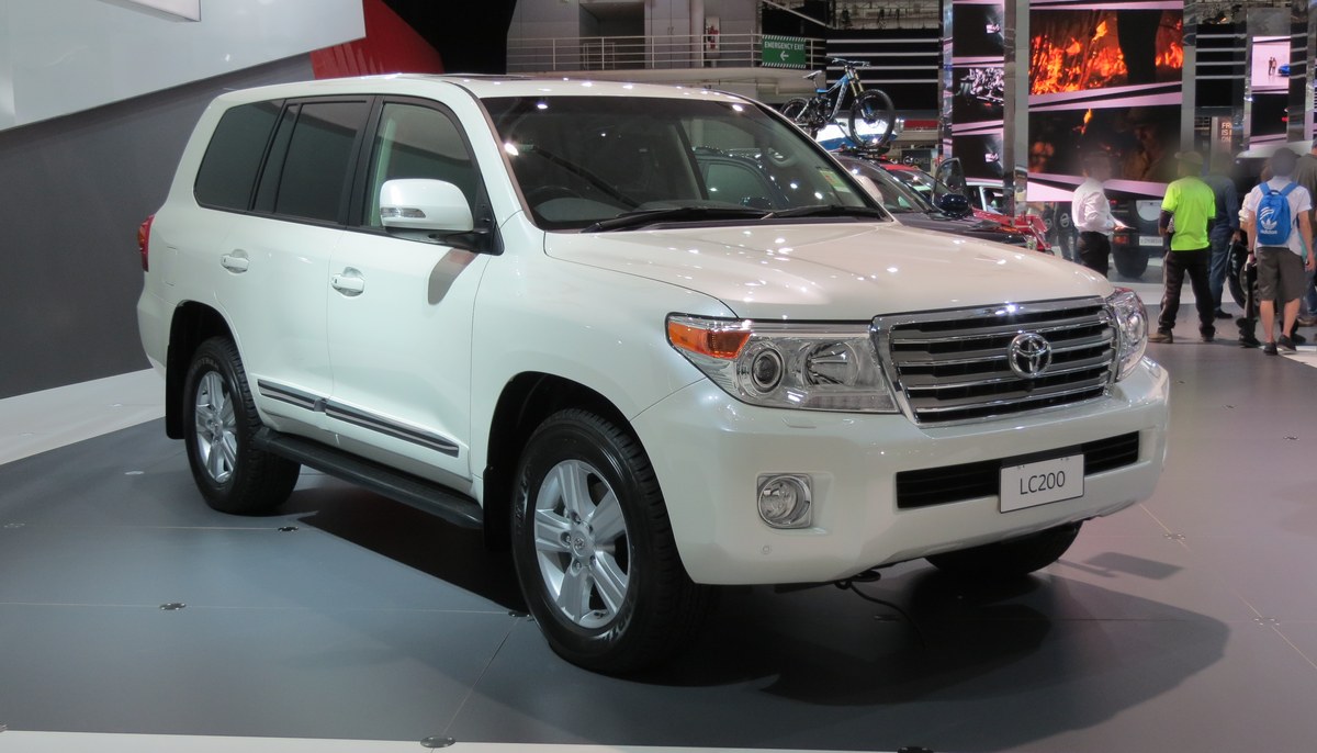 Белый Toyota Land Cruiser 200 на выставочной платформе, вид спереди в три четверти
