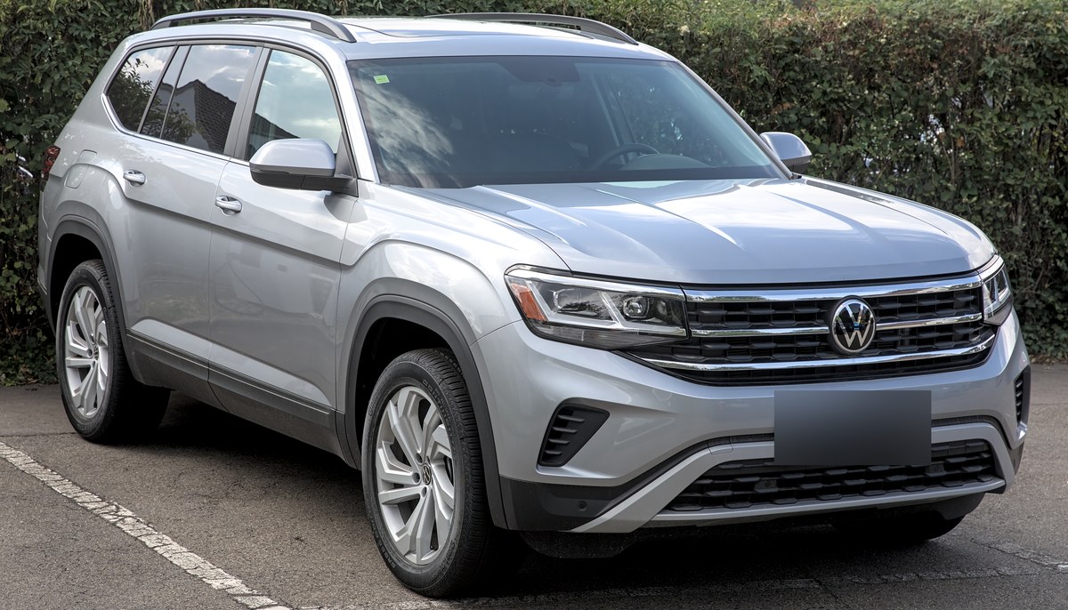 Серебристый Volkswagen Teramont (Atlas) рестайлинг, вид спереди сбоку на парковке у живой изгороди