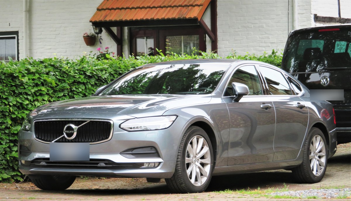 Серый седан Volvo S90 второго поколения у живой изгороди, вид спереди в три четверти